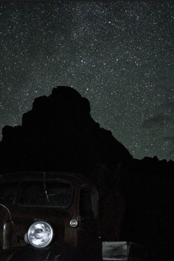 An aged truck stands proudly in the starry night, a testament to the passage of time and the beauty of the universe above