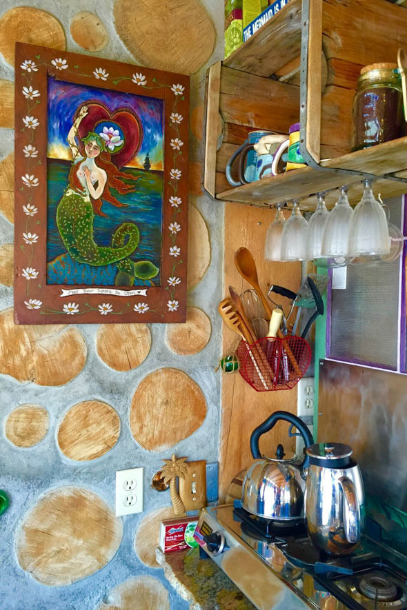 Experience the cozy ambiance of the Mermaid Cottage kitchen, featuring a delightful painting, a functional sink, and a stylish stove