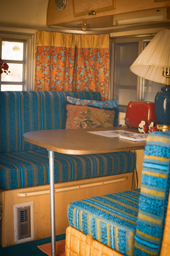 The Lucy Desi camper features a charming dining nook with a cozy table and chairs, ideal for enjoying meals or coffee