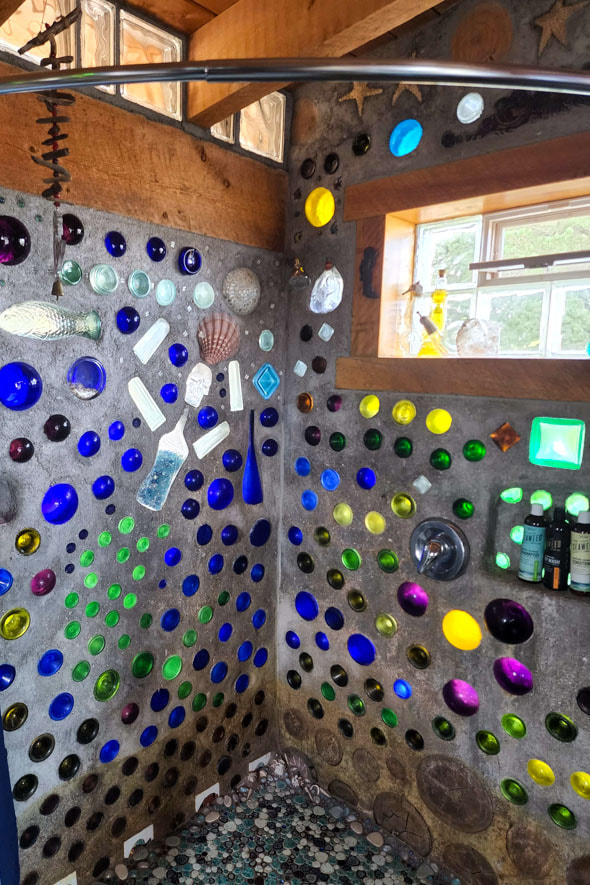 The mermaid cottage's bathroom features a shower with a glass bottle-covered wall