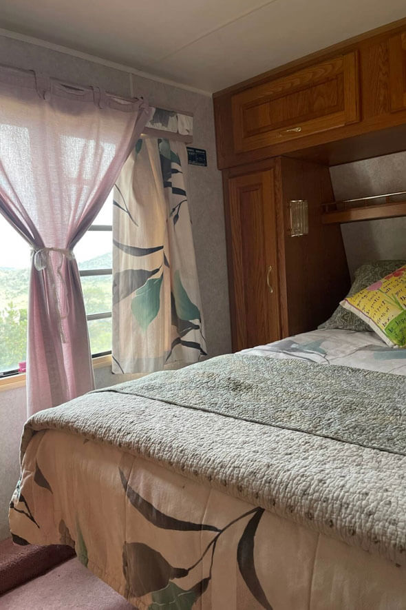 Cozy queen size bed in Holiday Rambler RV with curtains and window view